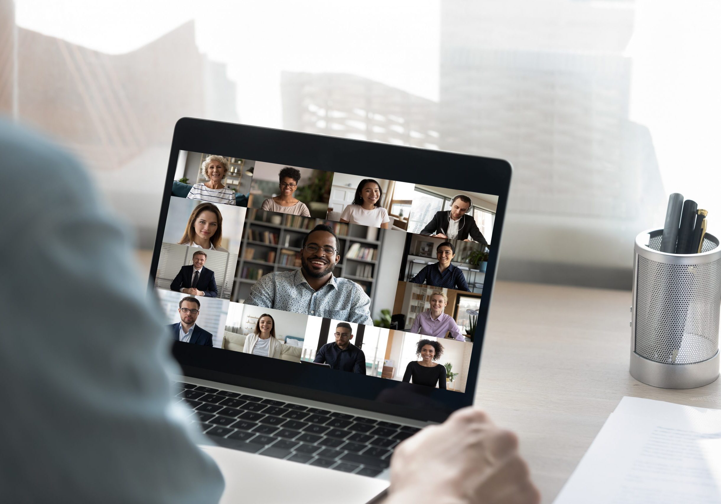 Back view of male employee have online video call on laptop with diverse multiethnic colleagues, man worker involved in webcam conference or virtual event on computer with multiracial businesspeople